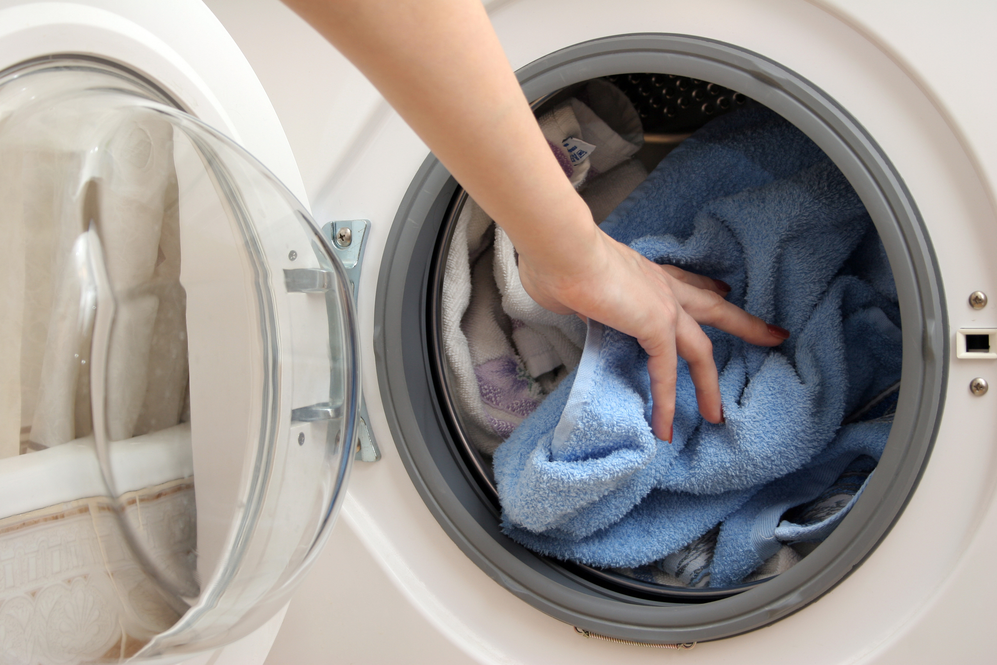 Hand Putting Towels On Washing Machine